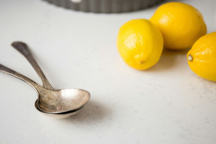 Three lemons and two spoons on a table.